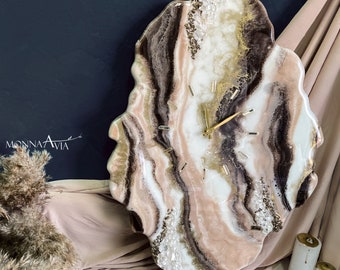 May include: A large, abstract wall clock with a white, pink, and brown resin face. The clock has a gold-colored frame and hands. The face of the clock is decorated with white and gold glitter.