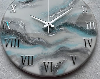 May include: A round clock with Roman numeral markings on a white background with blue and gray abstract resin art. The clock hands are silver.