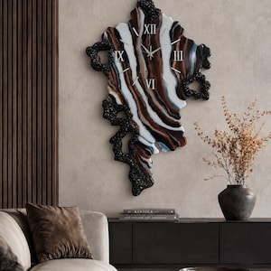 May include: A wall clock with an irregular, organic shape featuring a swirling pattern of white, brown, and blue resin. The clock face includes silver Roman numerals at the twelve, three, six, and nine o'clock positions and black textured edges.
