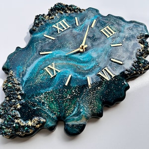 May include: A green and blue resin clock with gold Roman numeral markings and gold hands. The clock is shaped like an irregular, organic form.