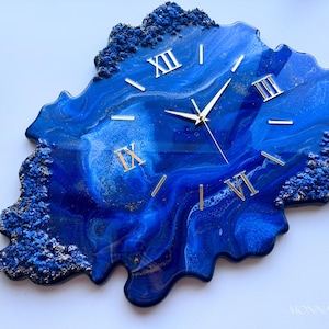 May include: Blue and gold resin wall clock with Roman numeral markings. The clock face is a unique abstract design with blue and gold swirls.
