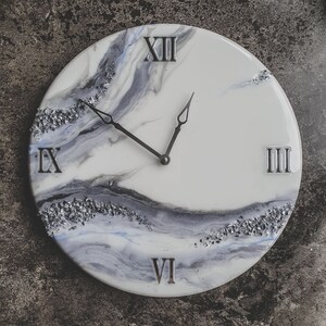 May include: A white clock face with black Roman numeral markings and silver glitter accents. The clock hands are black and the background is a white and gray marbled design.