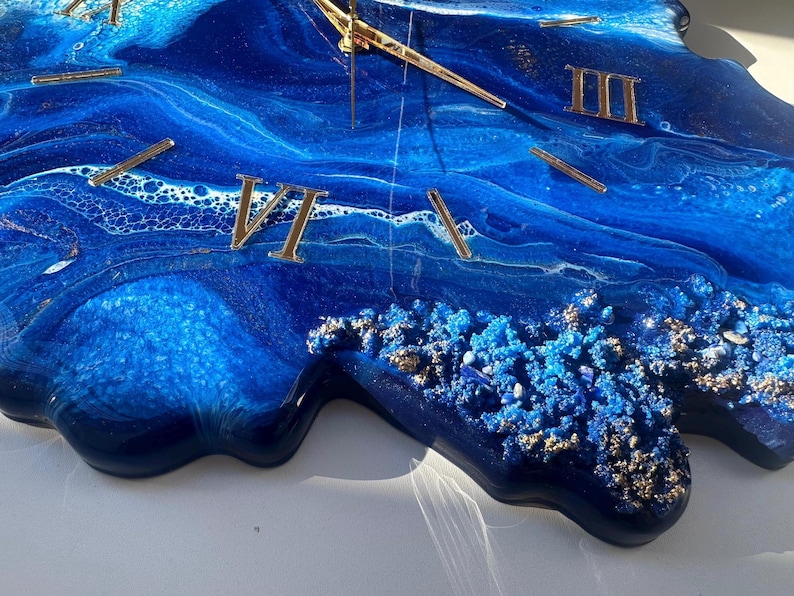 May include: A blue and gold resin clock with Roman numeral markings. The clock face is a swirling blue and white abstract design with gold glitter accents.