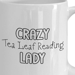 May include: White ceramic coffee mug with black text that reads "Crazy Tea Leaf Reading Lady".