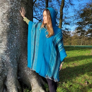 May include: A turquoise blue hooded poncho with a striped pattern. The poncho is made of a soft, warm material and has a fringed hem.