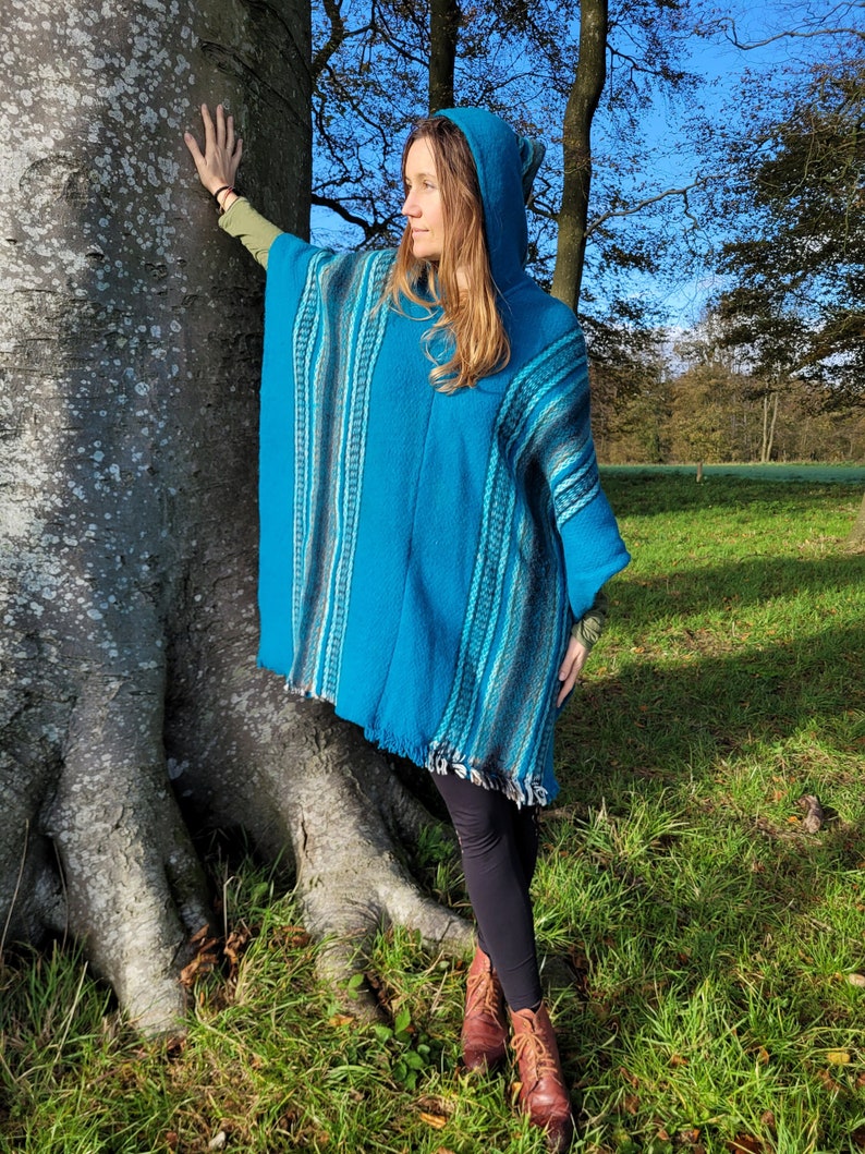 May include: A turquoise blue hooded poncho with a striped pattern. The poncho is made of a soft, warm material and has a fringed hem.