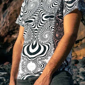 May include: A white t-shirt featuring a black and white abstract design. The pattern consists of swirling lines and shapes.