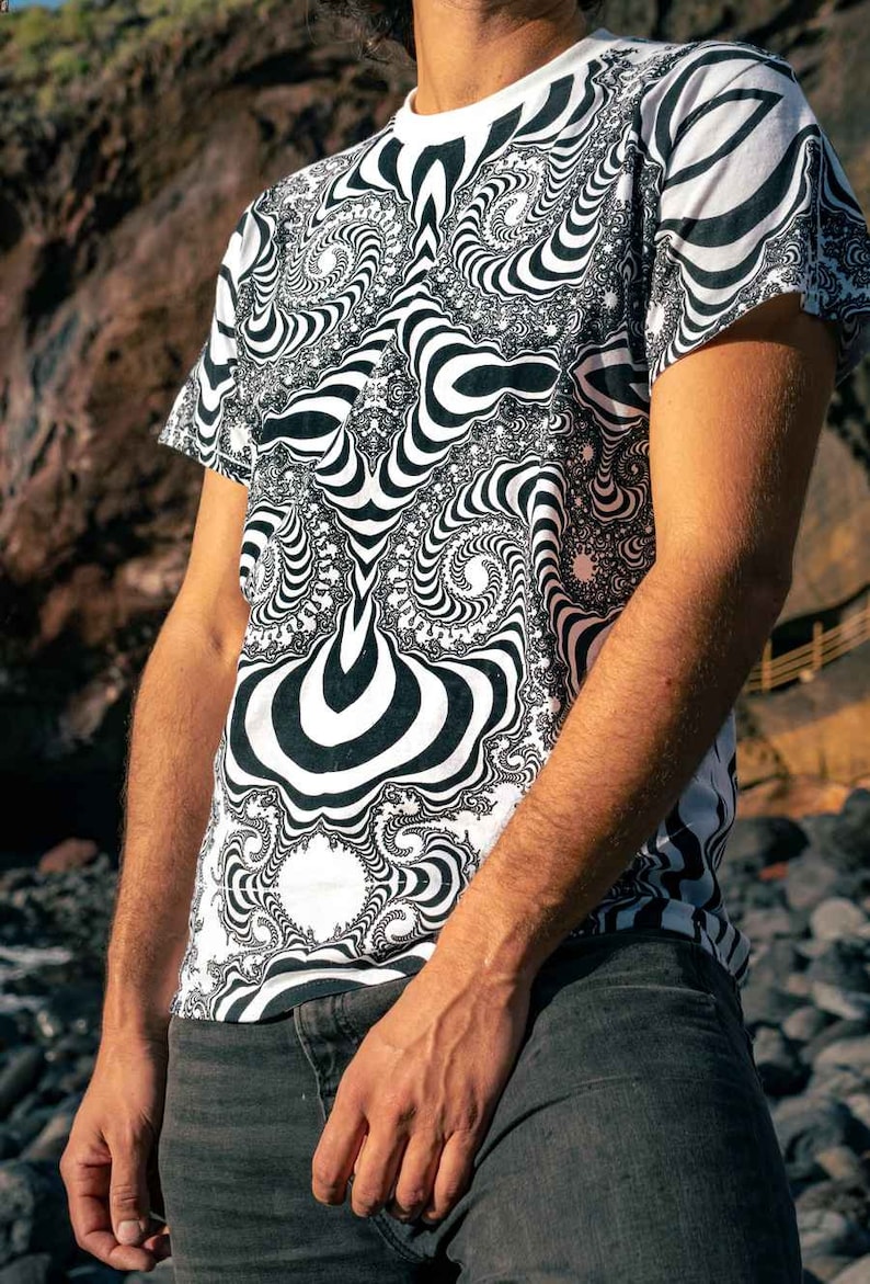 May include: A white t-shirt featuring a black and white abstract design. The pattern consists of swirling lines and shapes.