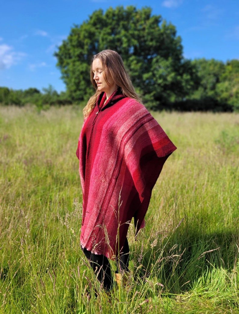 May include: A woman wearing a red hooded poncho with a striped pattern, standing in a field of tall grass.