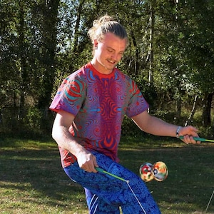 May include: A person wearing a red, blue and green patterned shirt and blue patterned trousers is juggling two colourful balls on strings.