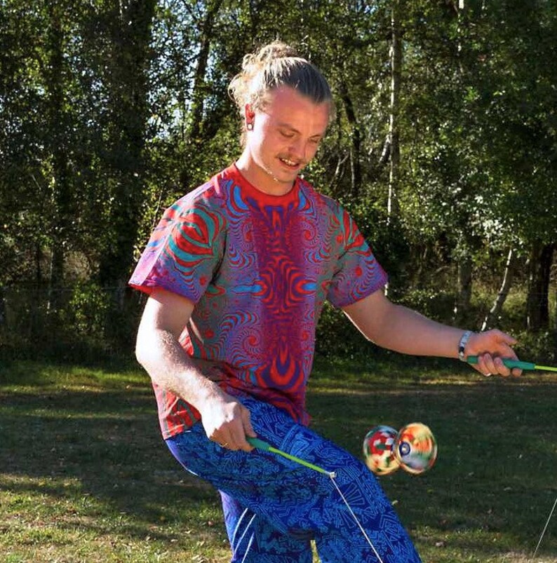 May include: A person wearing a red, blue and green patterned shirt and blue patterned trousers is juggling two colourful balls on strings.