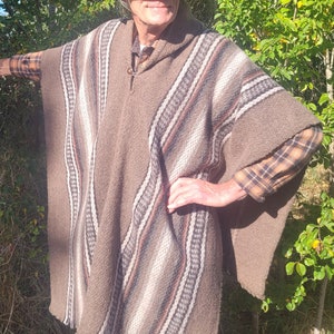 May include: A brown poncho with a striped pattern, worn by a person wearing a brown hat and a plaid shirt. The poncho has a hood and a fringe around the bottom.