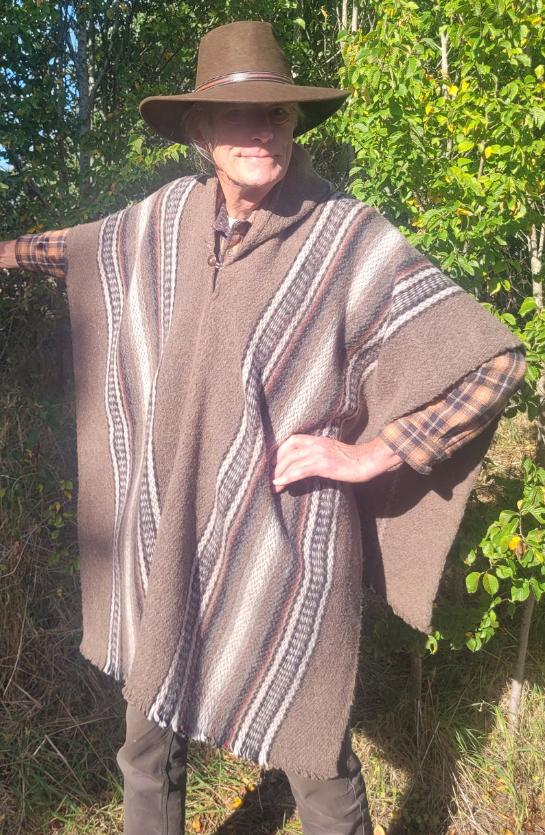 May include: A brown poncho with a striped pattern, worn by a person wearing a brown hat and a plaid shirt. The poncho has a hood and a fringe around the bottom.