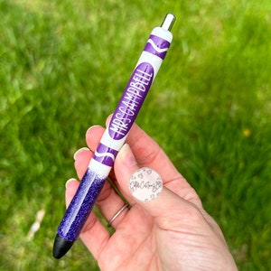 May include: Purple and white crayon-shaped pen with glitter accents. The pen has the text "Mrs. Campbell" printed on it.