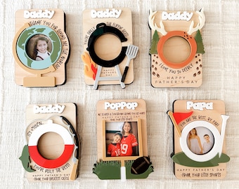May include: Six wooden photo frames with different designs and messages for Father's Day. The frames feature a globe, a grill, antlers, a life preserver, a football, and a golf club. Each frame has a space for a photo and a personalized message.