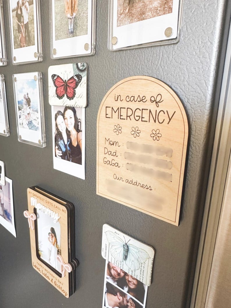 May include: A wooden sign with rounded edges and a white background. The sign says "in case of EMERGENCY" with a space for names and an address. The sign is attached to a refrigerator with magnets.