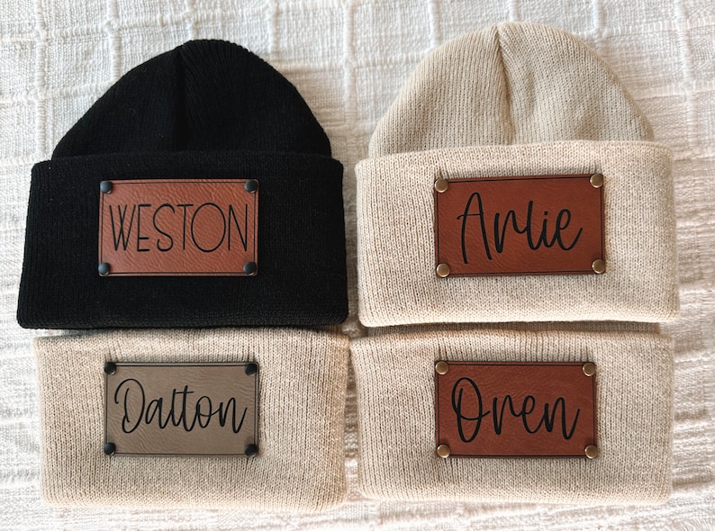 May include: Four knit beanies with leather patches. The beanies are in two colours: black and beige. The patches have the names Weston, Arlie, Dalton, and Oren.