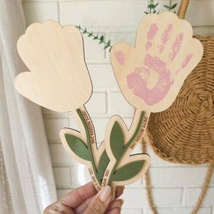 K&ouml;nnte beinhalten: Holzblumenf&ouml;rmiges Muttertagsgeschenk mit einem Handabdruck in rosa Farbe. Die Blume hat gr&uuml;ne Bl&auml;tter und Stiele mit dem Text "Happy Mother's Day" und "Love you always".