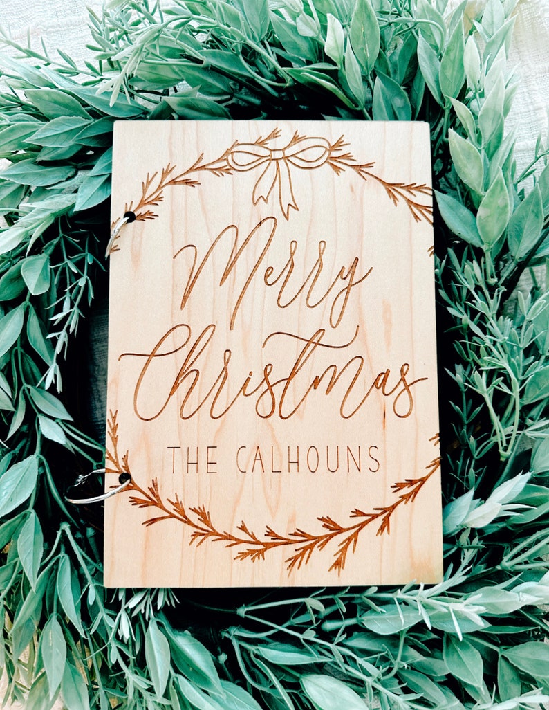 Pu&ograve; includere: Un cartello di legno con un design a corona di Natale e il testo "Merry Christmas The Calhouns".