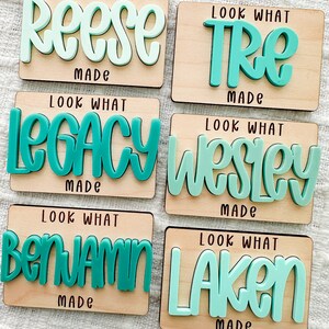 May include: Six wooden plaques with names in teal and light green, including "Reese," "Tre," "Legacy," "Wesley," "Benjamin," and "Laken." Each plaque has the text "Look What Made" in black.