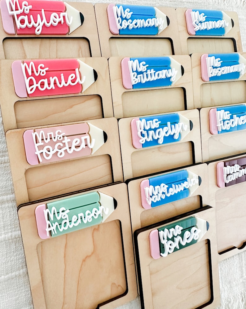 May include: A set of 10 wooden name tags with pencil-shaped frames. Each frame has a different color and features a name in white lettering. The names include: Ms. Taylor, Ms. Rosemary, Ms. Sunmon, Ms. Daniel, Ms. Brittany, Ms. Rosemary, Mrs. Foster, Mrs. Singelyn, Ms. Anderson, Mrs. Jones.
