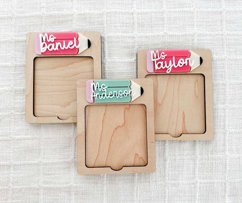 May include: Three wooden frames with a pencil design and a name on each. The names are Ms. Daniel, Ms. Taylor, and Ms. Anderson. The frames are light brown and have a white background.