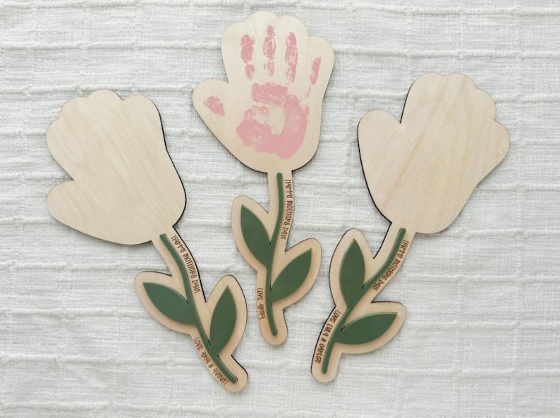 K&ouml;nnte beinhalten: Holzblumen-Ausschnitte mit gr&uuml;nen Stielen und Bl&auml;ttern. Eine Blume hat einen rosa Handabdruck. Die Stiele tragen die Aufschrift "Happy Mother's Day" und "Love you forever".