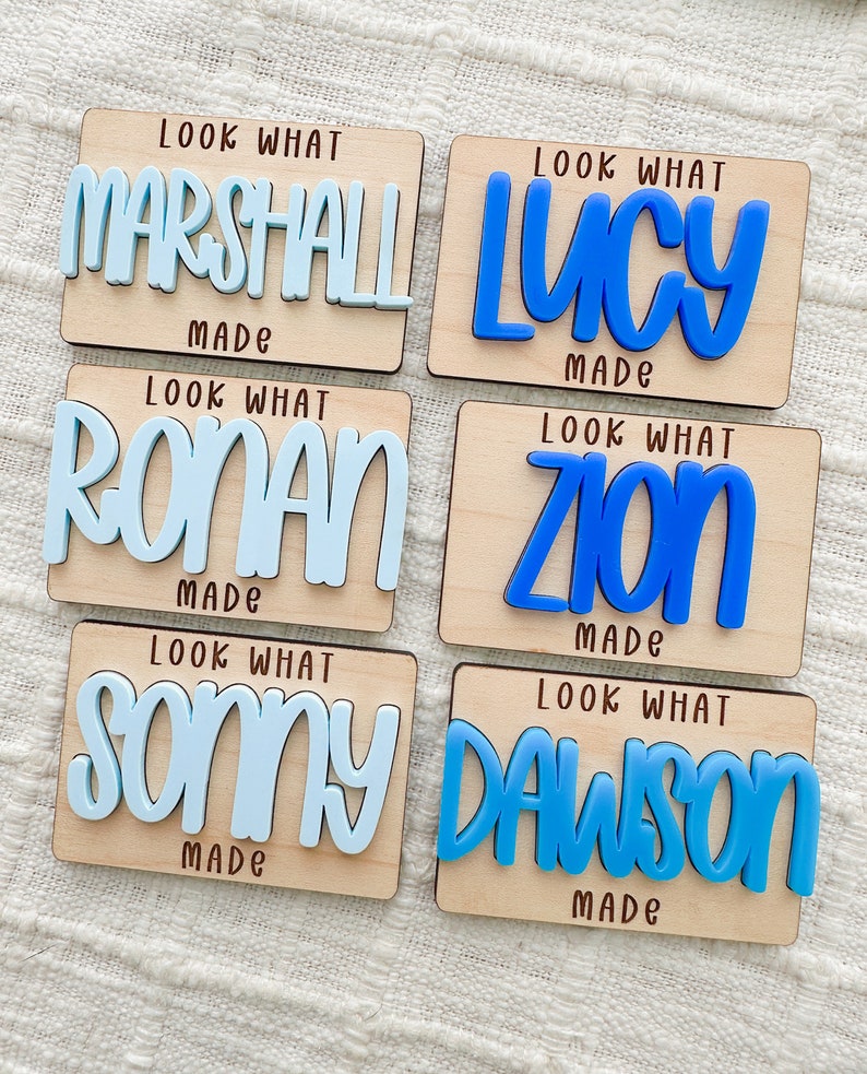 May include: Six wooden name plaques with the text "Look What Made" and a name in blue. Names include Marshall, Lucy, Ronan, Zion, Sonny, and Dawson. The names are in a bold, playful font.