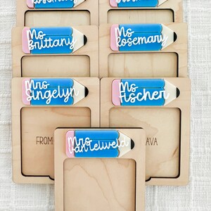 May include: Set of six wooden frames with a pencil-shaped cutout. Each frame has a different teacher's name written on it in white lettering. The frames are arranged in two rows of three. The top row reads "Ms. Rosemary", "Ms. Surmon", and "Ms. Brittany". The bottom row reads "Mrs. Singelyn", "Ms. Fischer", and "Mrs. VanTelweld".