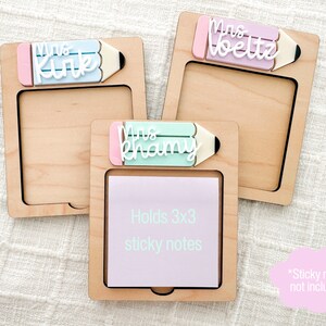 May include: Three wooden note holders with a pencil design and a space for 3x3 sticky notes. The holders are personalized with the names "Mrs. Kirk", "Mrs. Khamy", and "Mrs. Voeltz".