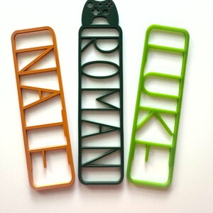May include: Three colourful bookmarks with cut-out letters spelling "NAIL", "ROMAN", and "LURE". The "ROMAN" bookmark has a small game controller at the top.
