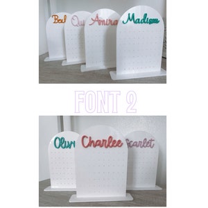 May include: Two white earring stands with different fonts. The top stand has the names Bexl, Quy, Amira, and Madizon in different colours. The bottom stand has the names Olivi, Charlee, and Scarlet in different colours. The text "ALL EARRING STANDS COME WITH FONT 1 AUTOMATICALLY, IF YOU WOULD LIKE TO SWITCH TO FONT 2 PLEASE ADD A NOTE WITH THE NAME IN THE PERSONALIZATION BOX (" is below the stands.