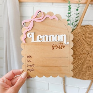 May include: Wooden baby announcement plaque with a pink bow and the names Lennon Faith. The plaque has spaces to record the date, time, weight, and length of the baby.