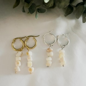 Puede incluir: Dos pares de pendientes de aro con colgantes hechos de pequeñas cuentas de piedra irregulares de color blanco roto. Un par de pendientes tiene aros de metal dorado, mientras que el otro par tiene aros de metal plateado, ambos con herrajes a juego.