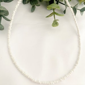 Peut inclure: Un d&eacute;licat collier de perles blanches. Le collier est compos&eacute; de petites perles blanches rondes enfil&eacute;es ensemble. Le fermoir et la cha&icirc;ne sont de couleur dor&eacute;e. Le collier est pr&eacute;sent&eacute; sur un fond blanc avec du feuillage vert.