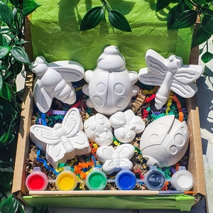 Puede incluir: Un conjunto de ocho figuritas de cer&aacute;mica blanca en forma de mariquita, mariposa y lib&eacute;lula en una caja de cart&oacute;n con botes de pintura y un pincel. Las figuritas est&aacute;n listas para ser pintadas.