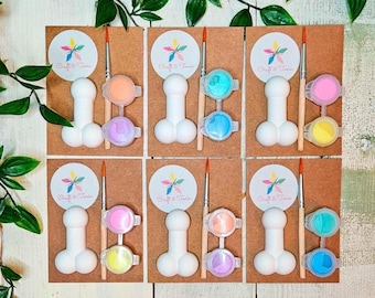 May include: Six craft kits on brown cardboard backing, each featuring a white phallic-shaped ceramic figure, a wooden paintbrush, and two small circular paint pots in various colors, with a circular logo reading Craft & Tonic.
