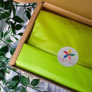 May include: A cardboard box with a green tissue paper lining. The box is open and the tissue paper is visible. A white circle sticker with the text "Craft & Tonic" and a colorful flower design is on the tissue paper.