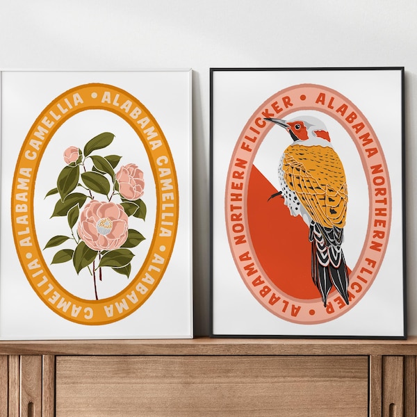 May include: Two framed art prints. One features a camellia flower illustration with the text "Alabama Camellia" in a circular design. The other print depicts an Alabama Northern Flicker bird with the same circular text design.