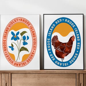 Op de afbeelding: Twee ingelijste kunstdrukken. Eén toont blauwe viooltjes met de tekst "Rhode Island Violet" in een cirkelvormig ontwerp. De andere print toont een bruine kip met de tekst "Rhode Island Red" in een cirkelvormig ontwerp. Beide prints hebben een witte achtergrond.
