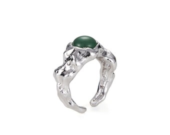 May include: A silver ring with a textured, organic design. The ring features a green gemstone set in the center.