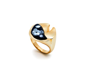 May include: A gold ring with a black and white stone set in a unique, abstract shape.