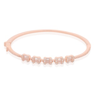 Könnte beinhalten: Ein roségoldenes Armreif-Armband mit einer Reihe von fünf rechteckigen Clustern aus klaren Zirkonia-Steinen.
