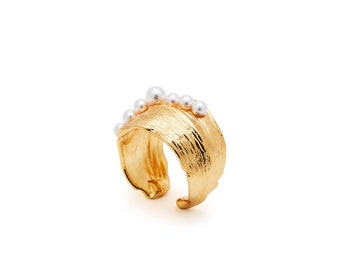 May include: A gold ring with a textured, leaf-shaped band and a row of white pearls.