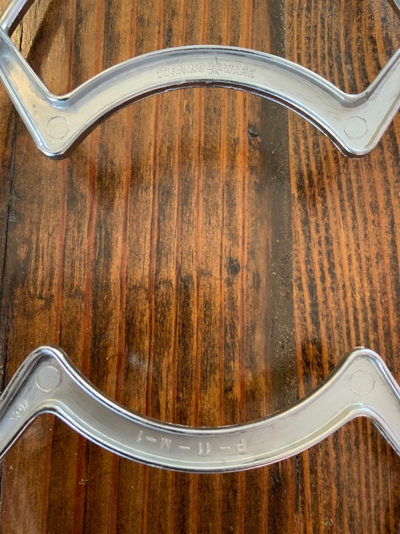 May include: Two silver metal stovetop burner rings with the text "CORNING WARE" and "P-11-M-J" on them.