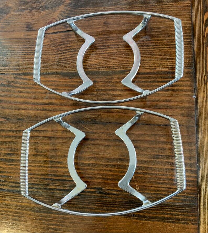May include: Two silver metal hot pad trivets with a wavy design. The trivets are oval shaped and have a raised edge.