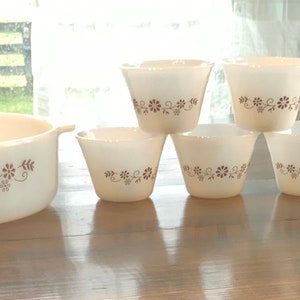 May include: A set of white Pyrex baking dishes with a brown floral pattern. The set includes a large oval baking dish and four smaller round dishes.