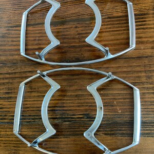 May include: Two silver metal cooling racks for hot dishes. The racks are oval shaped with a handle on each side.