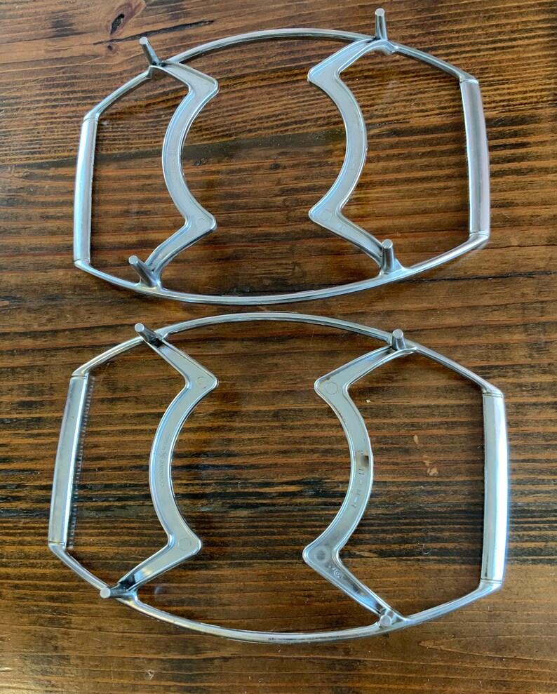 May include: Two silver metal cooling racks for hot dishes. The racks are oval shaped with a handle on each side.