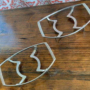May include: Two silver metal hot plate stands with a wavy design. The stands are on a wooden surface.